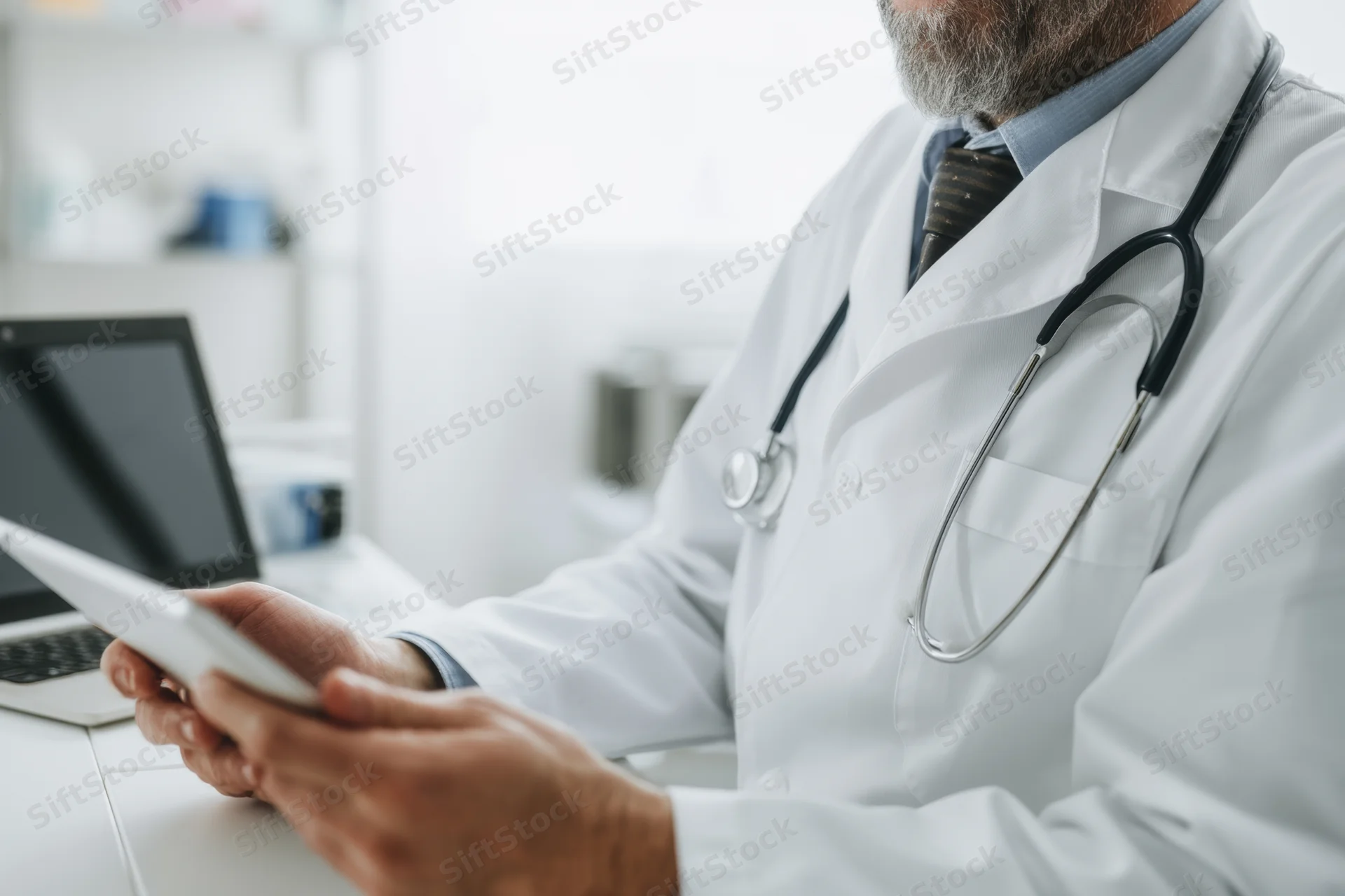 Doctor in white coat using tablet at desk in clinic office