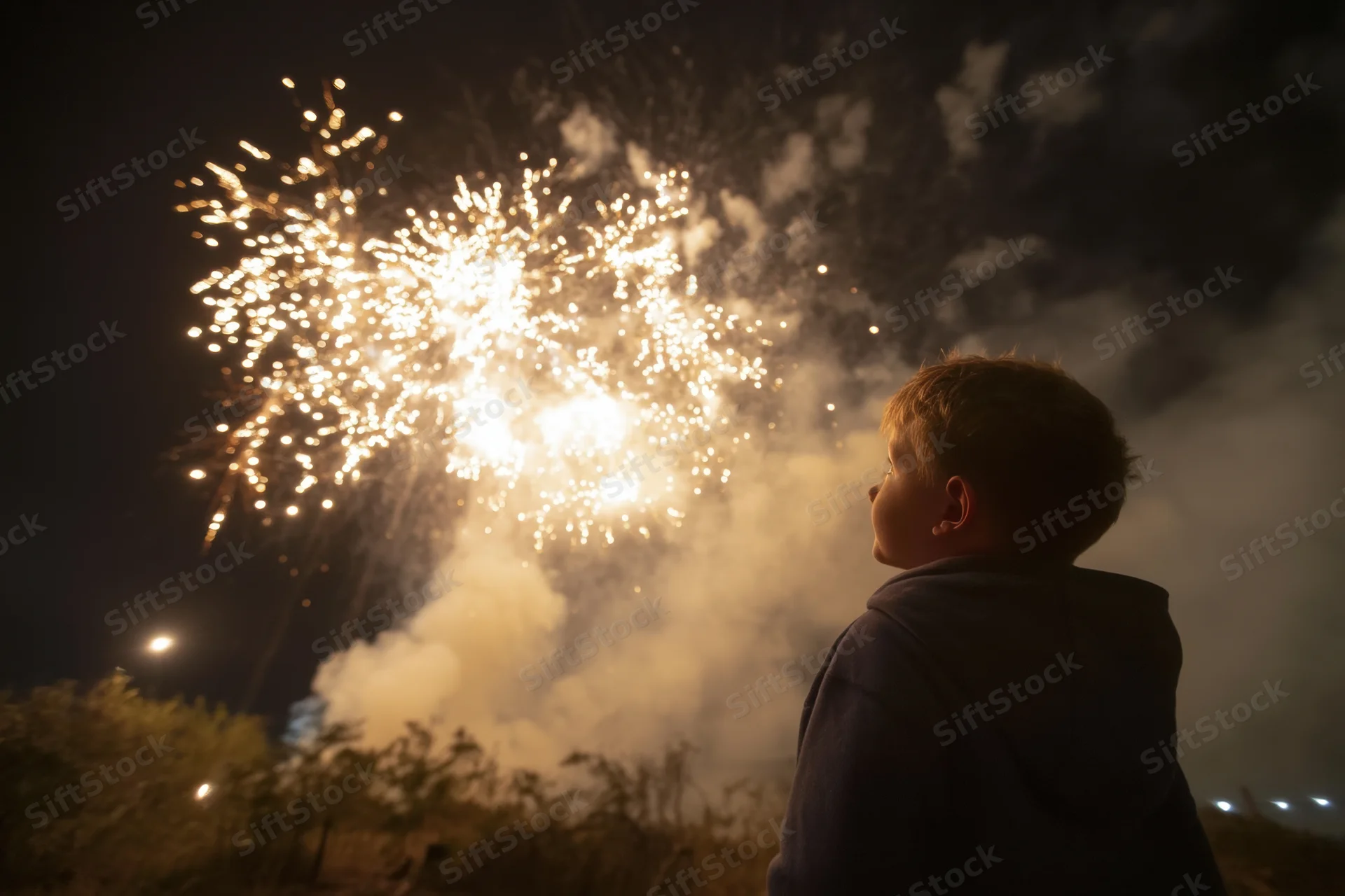 Young boy in silhouette watching fireworks explode in the night sky