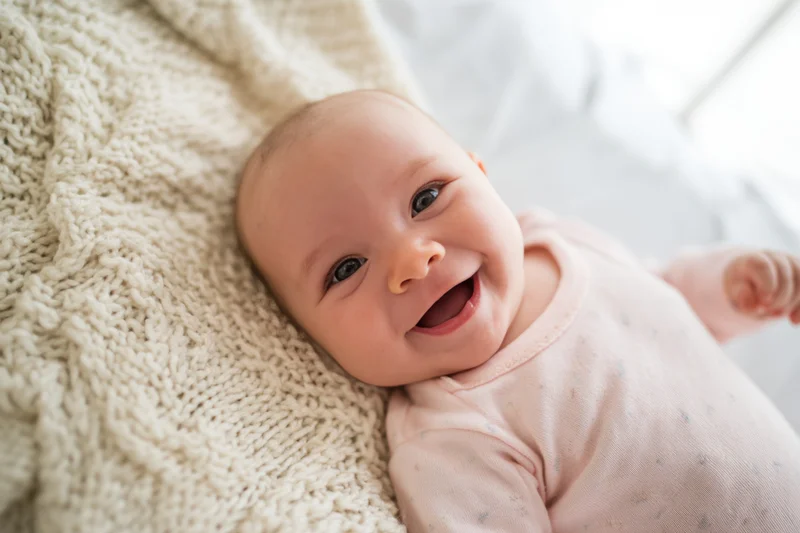 Smiling baby lying on cream knitted blanket wearing pale onesie