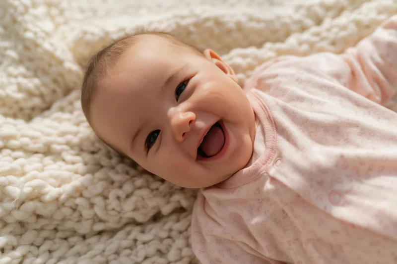 Smiling baby lying on cream knitted blanket wearing pink onesie