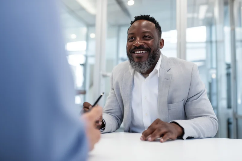 Smiling businessman in light gray blazer sitting at white table during office meeting