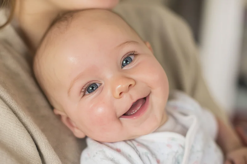 Smiling baby held in caregiver's arms close-up