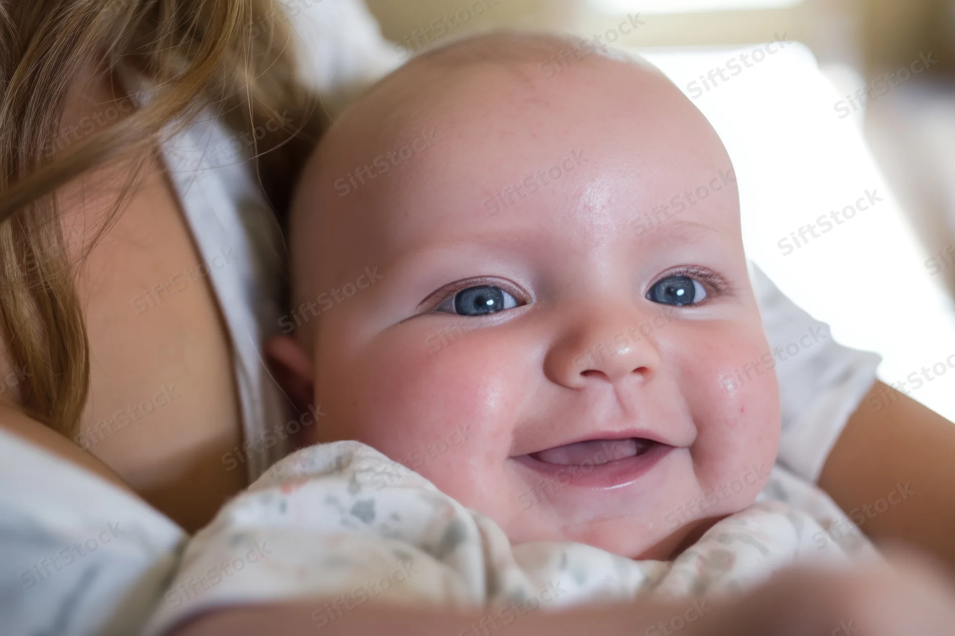 Smiling baby held in mother's arms close-up indoors
