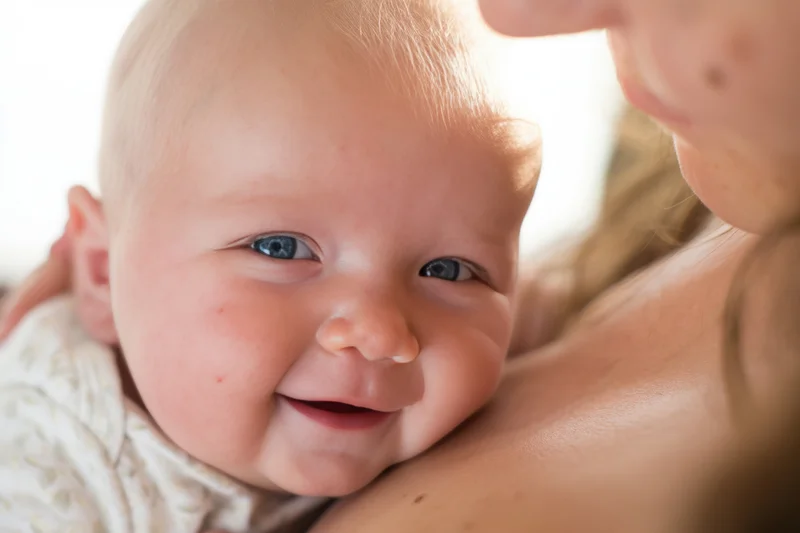 Smiling infant resting on caregiver's shoulder in close-up portrait