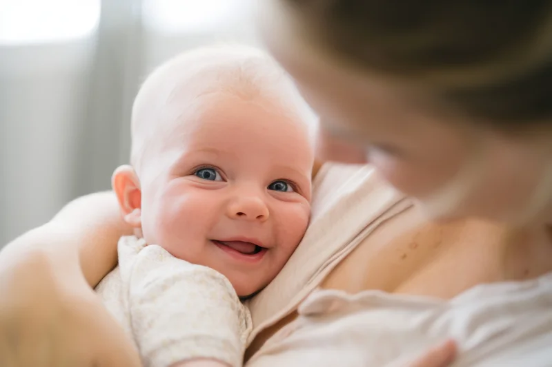 Smiling baby held in mother's arms close up indoors