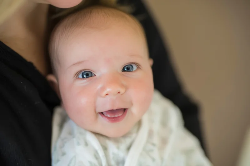 Smiling baby held close in caregiver’s arms indoors