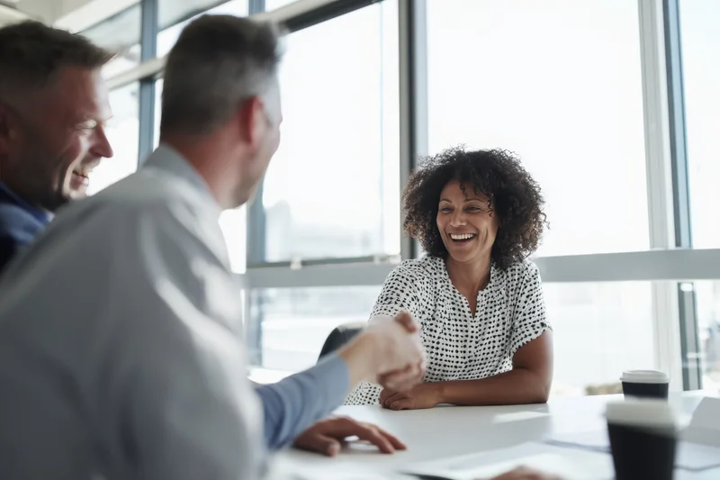 Woman and man shaking hands across conference table in office meeting