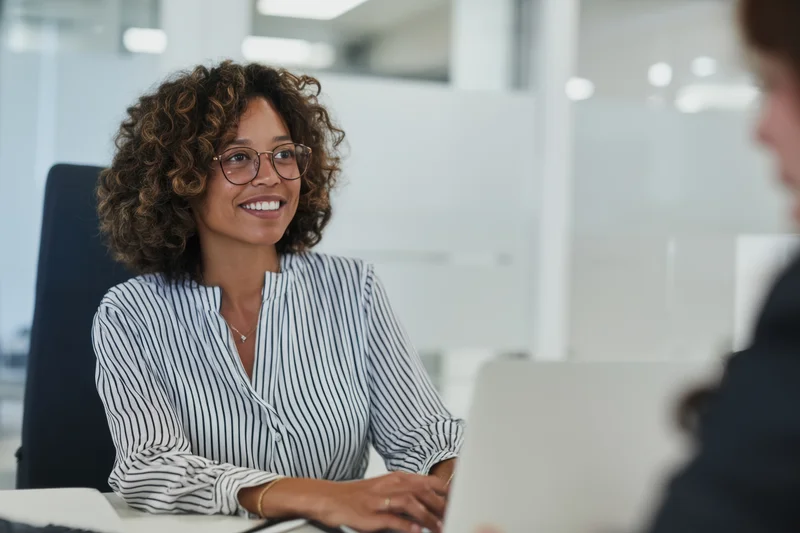 Woman smiling during office meeting at desk with laptop