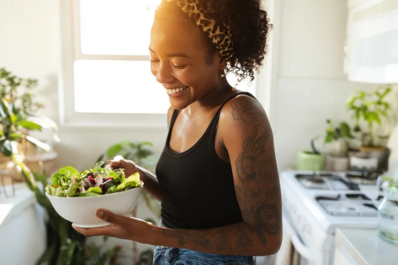 Smiling woman holding a bowl of salad in a bright kitchen