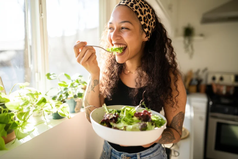 Woman eating a salad in a bright kitchen with potted plants near the window