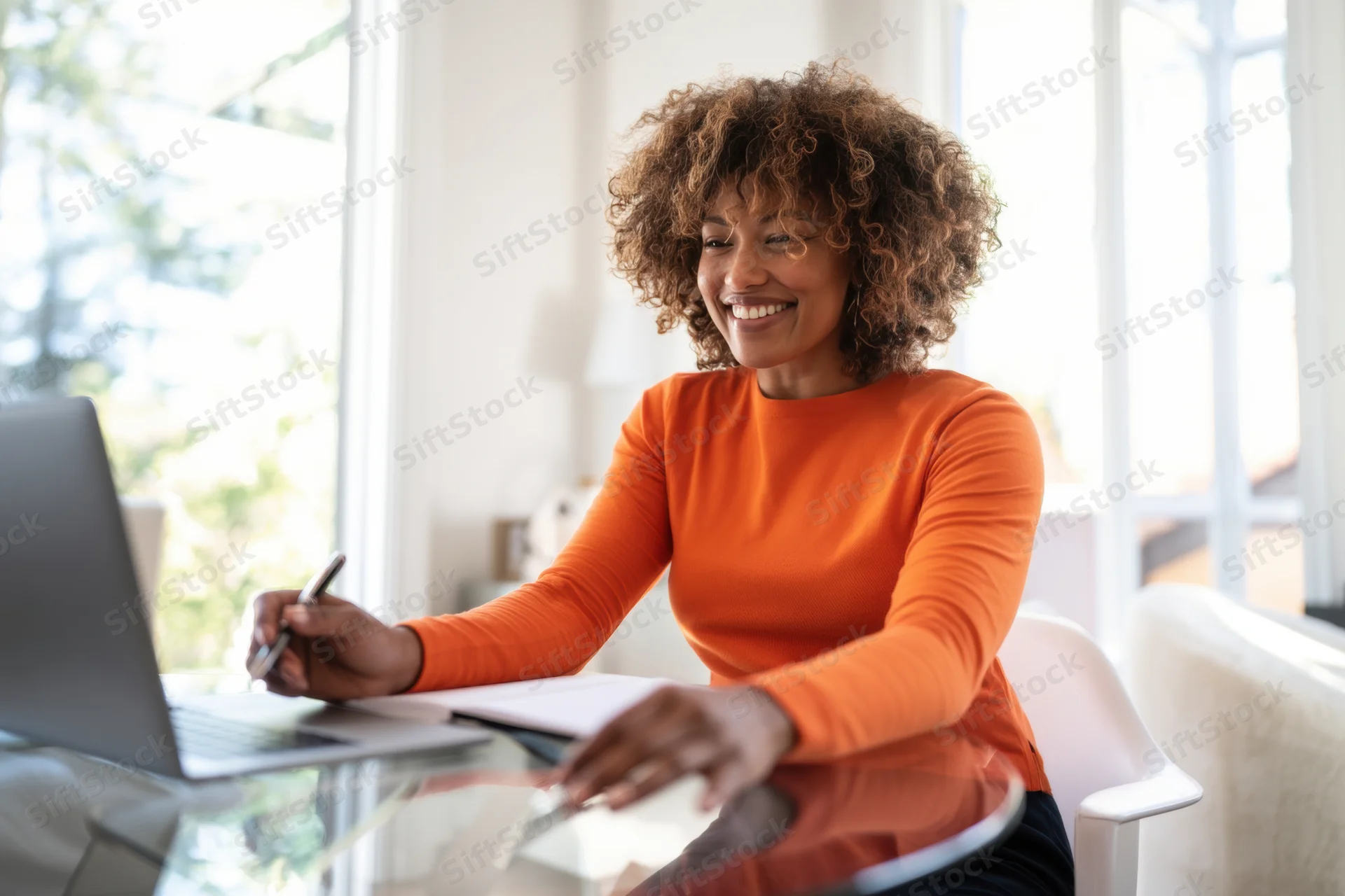 Woman smiling while working on laptop at glass desk in home office