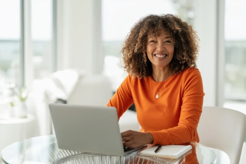 Smiling woman with curly hair working on laptop at glass desk in bright modern office