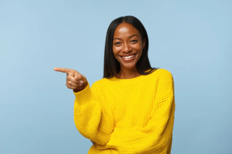 Smiling woman in yellow sweater pointing to the side against blue background