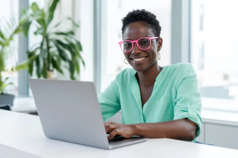 Smiling woman using laptop at desk in bright office space