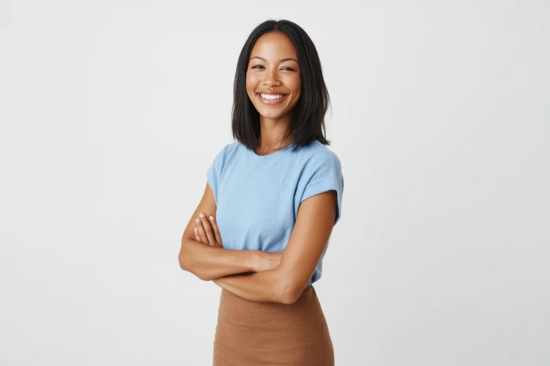 Smiling woman with arms crossed in a blue t-shirt and brown skirt against a white background