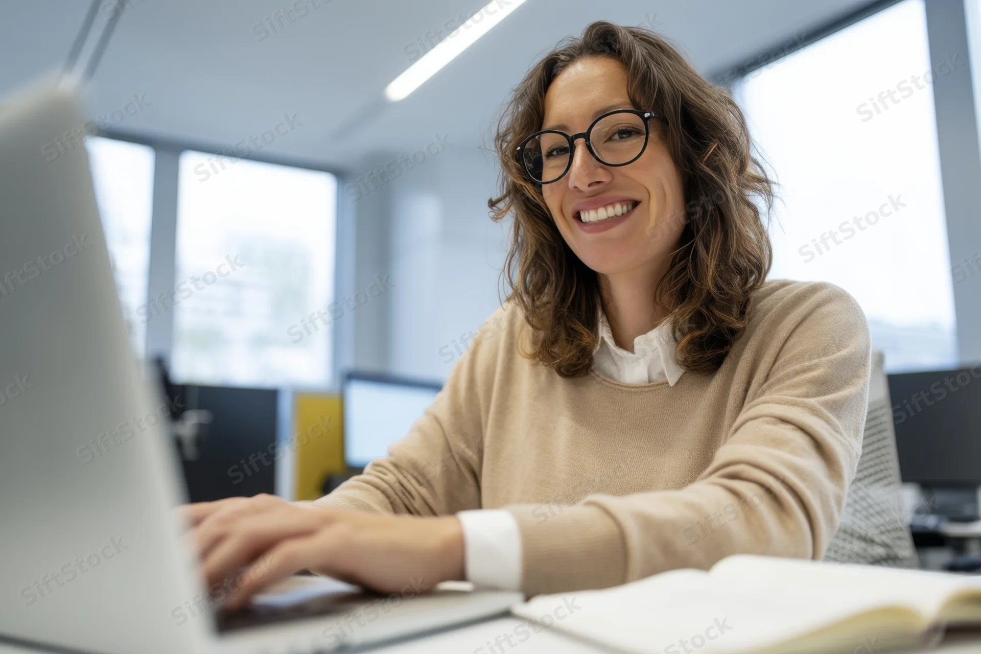 Woman smiling while typing on laptop at office desk