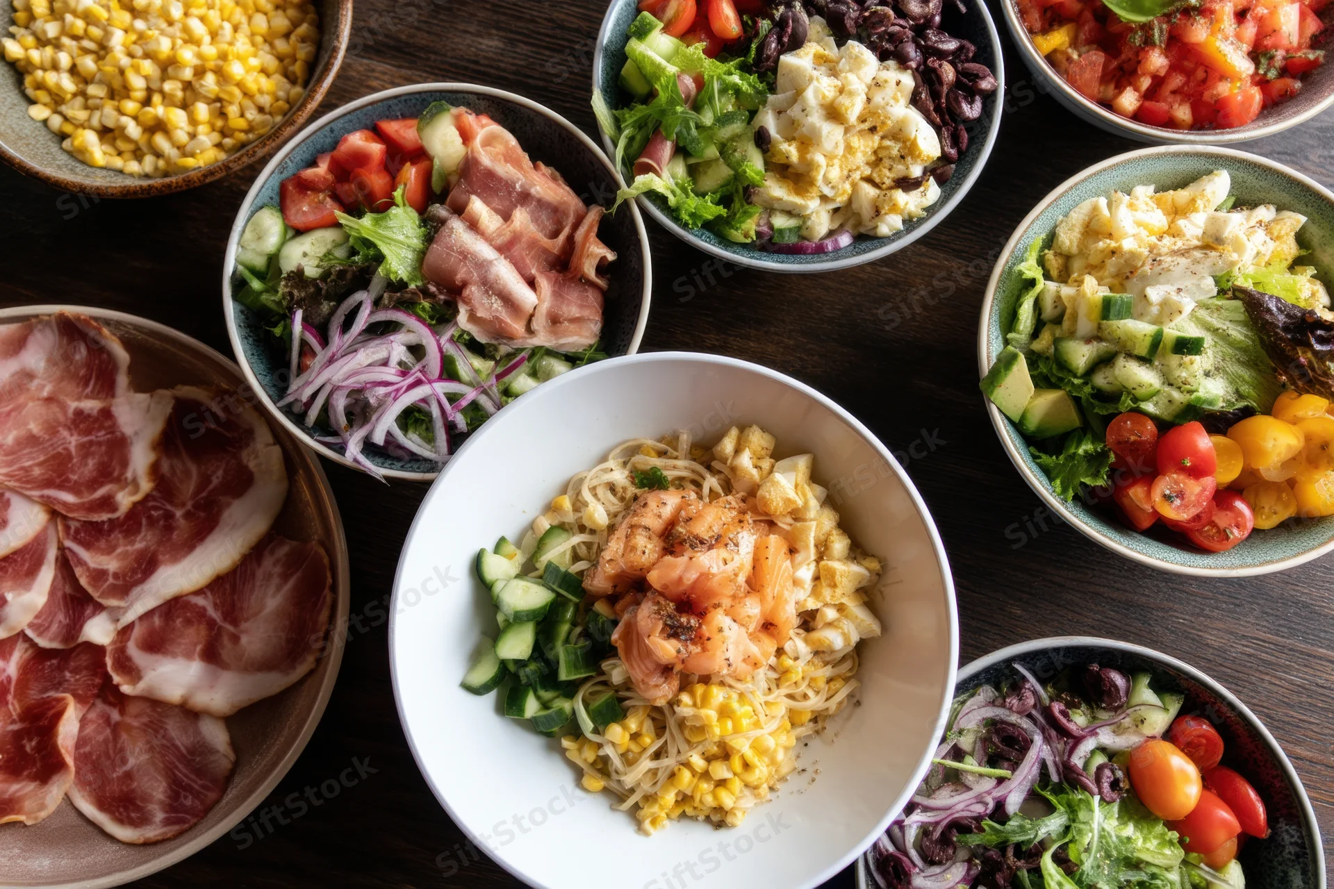 Overhead view of multiple bowls filled with colorful salads and pasta dishes arranged on a dark wooden table