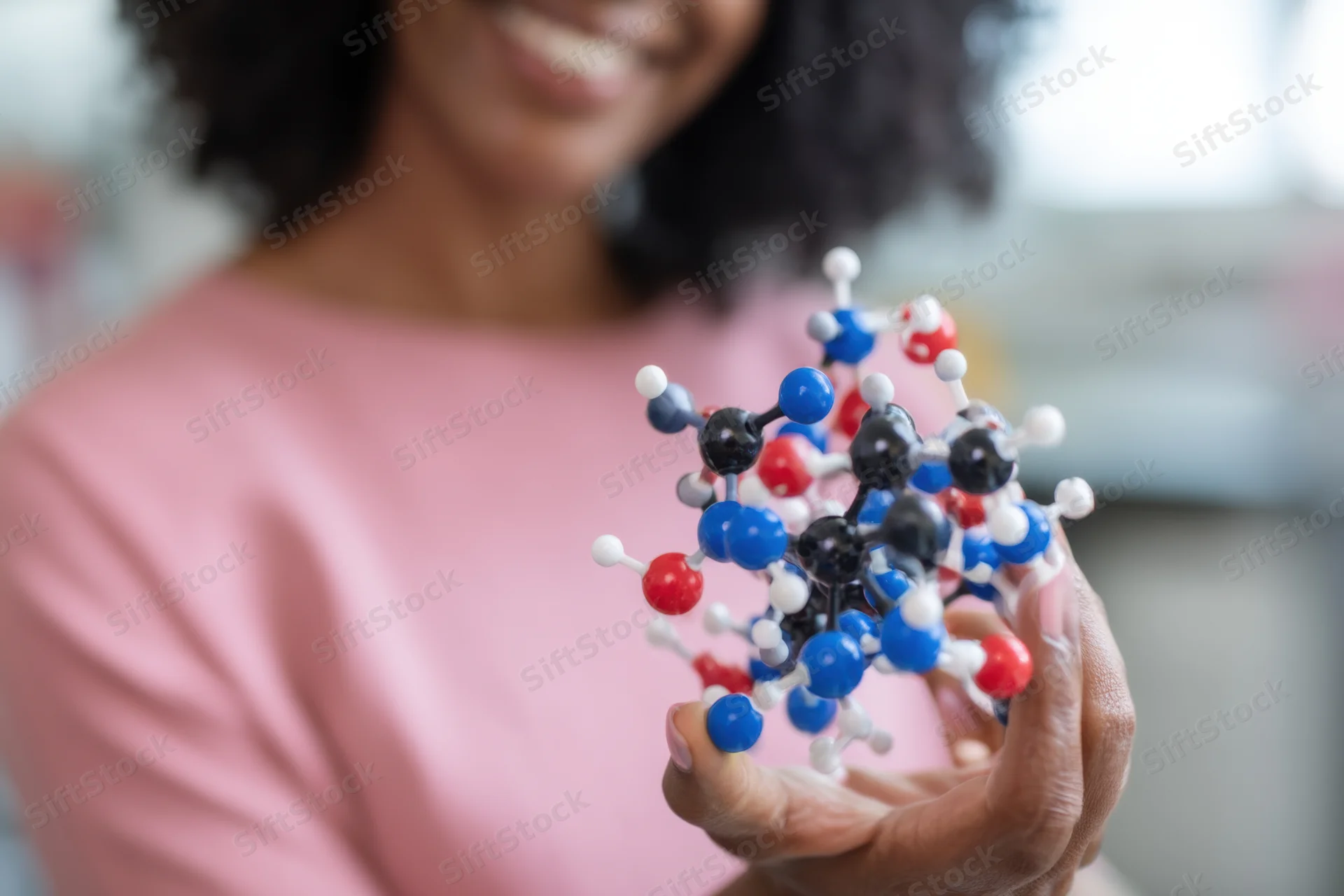 Woman holding a colorful molecular model close to the camera in a classroom setting