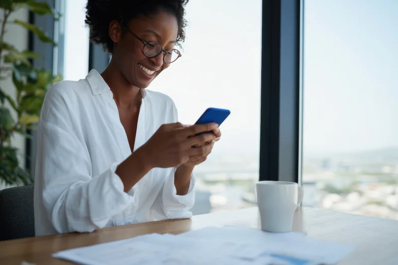 Woman smiling while using smartphone at office desk by window