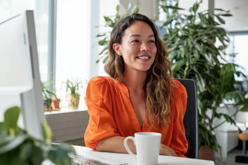 Woman smiling at desk in office with computer and plants