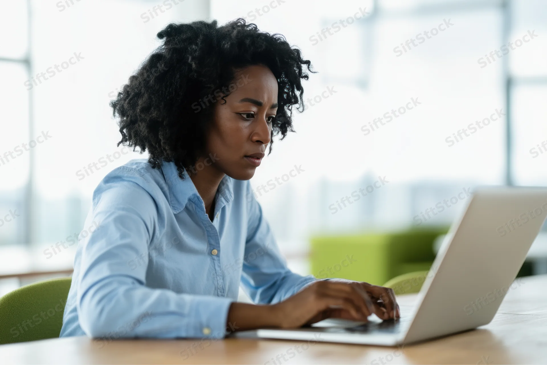 Woman working on laptop at wooden desk in office with window view