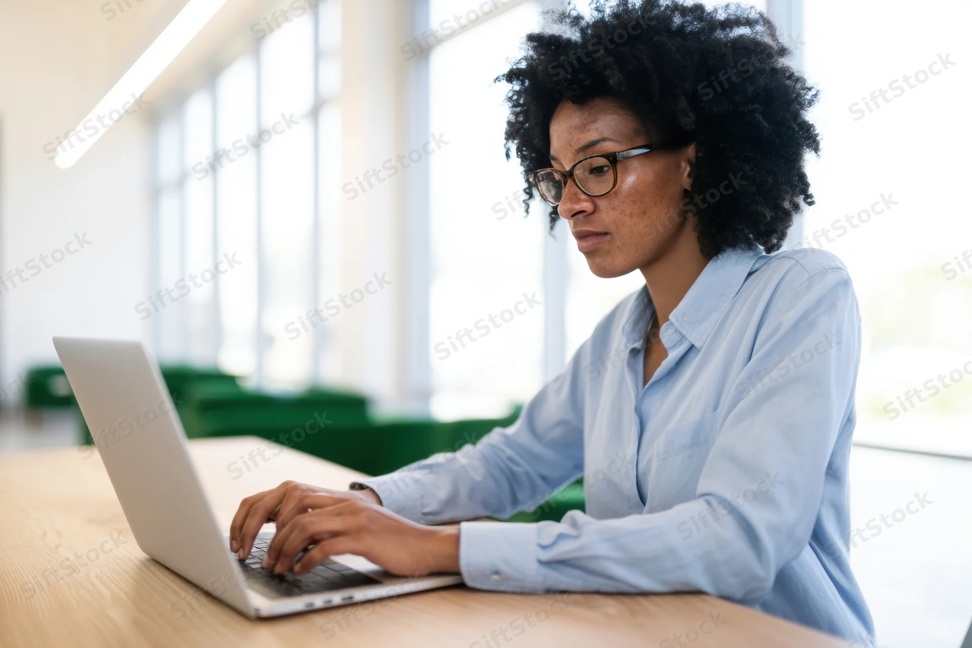 Woman typing on laptop at wooden desk in bright office space