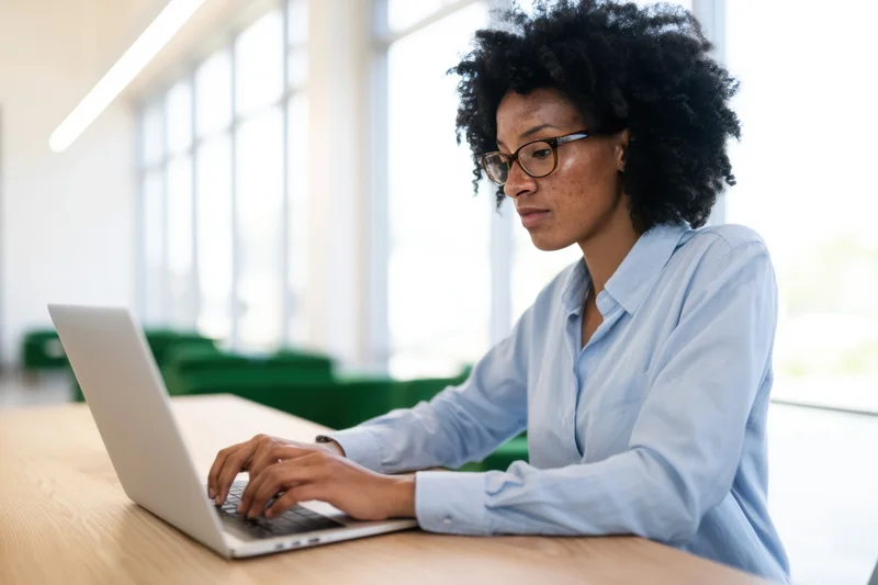 Woman typing on laptop at wooden desk in bright office space