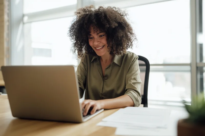 Woman smiling while typing on laptop at wooden desk in office