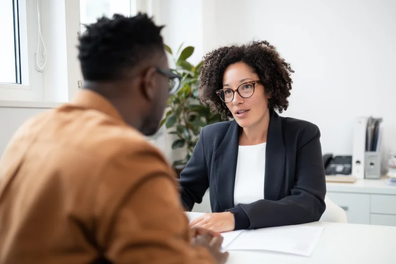 Woman in dark blazer discussing with man at office desk