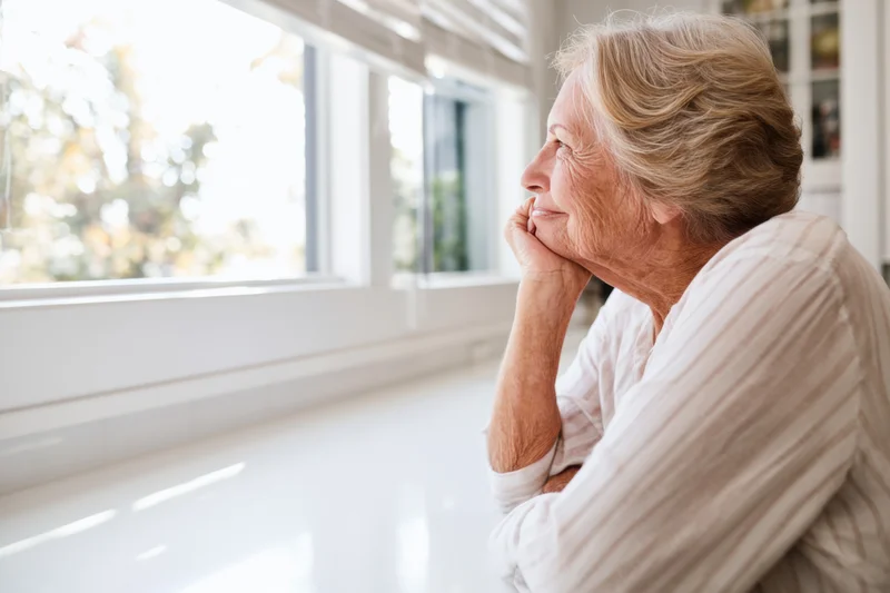 Elderly woman smiling while gazing out kitchen window in bright home interior