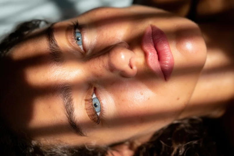 Close-up of a woman lying on her side with blue eyes in sunlight and shadow