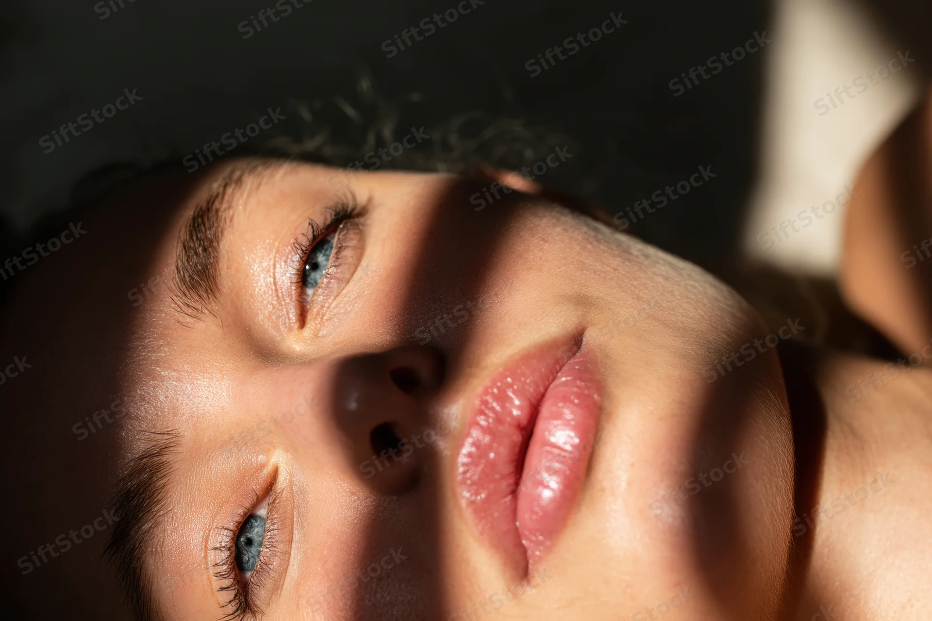 Closeup of a woman lying on her side with blue eyes gazing upward in sunlight and shadow
