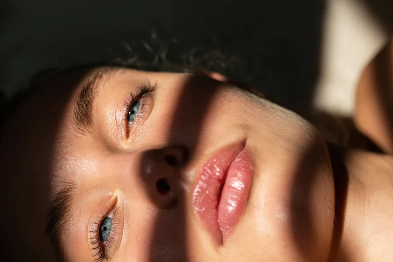 Closeup of a woman lying on her side with blue eyes gazing upward in sunlight and shadow
