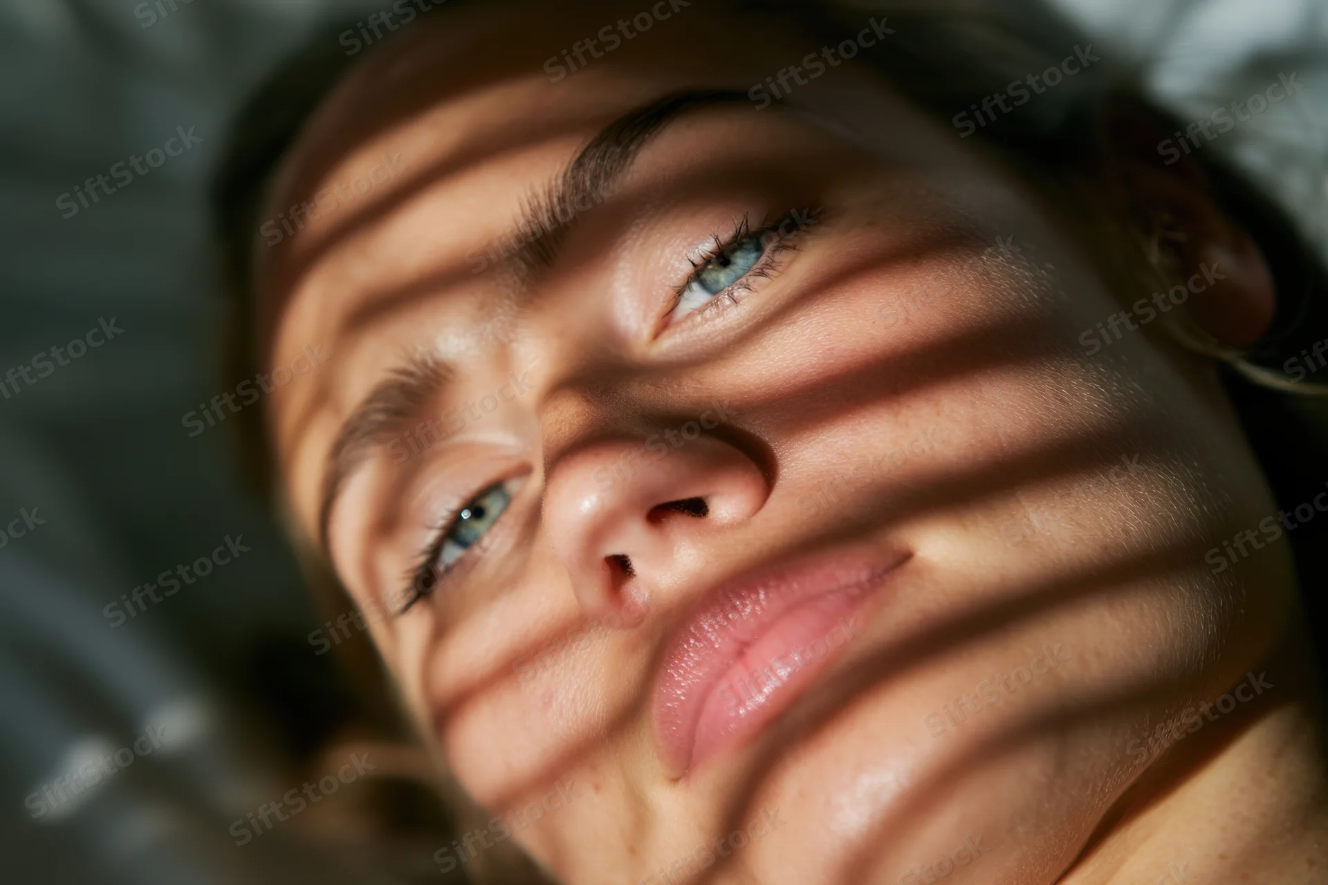 Woman lying on side with sunlight and shadows on her face in bedroom