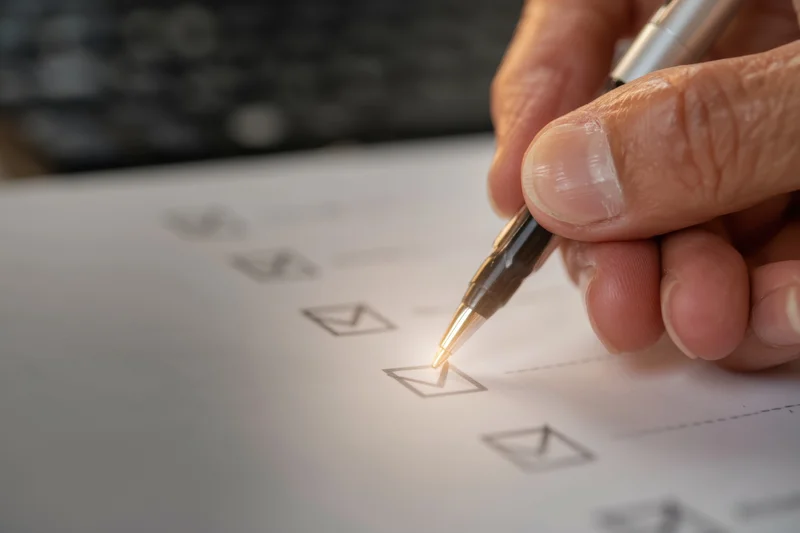 Hand marking a checkbox on a document with a pen in an office setting
