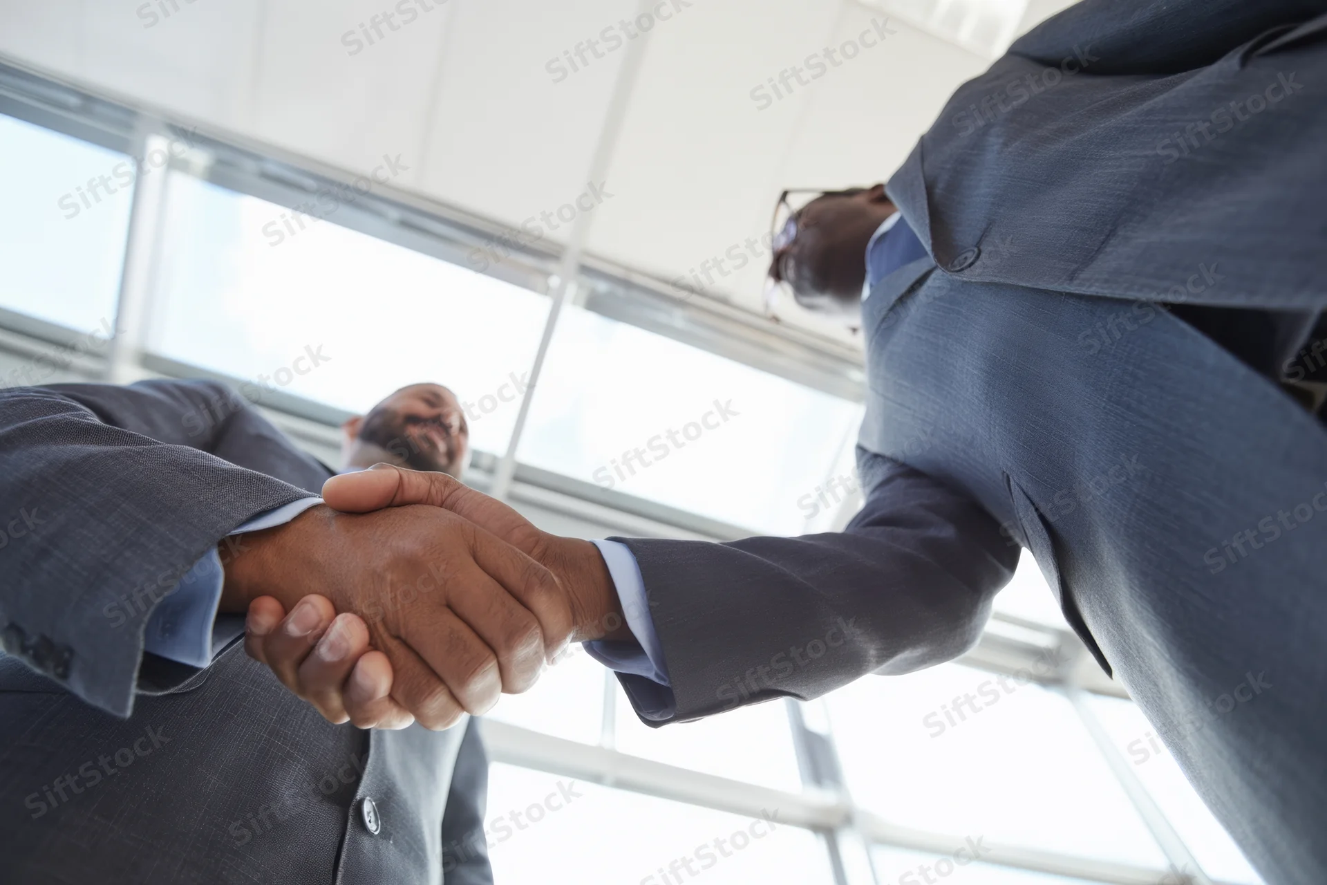 Two men in suits shaking hands in a modern office with large windows