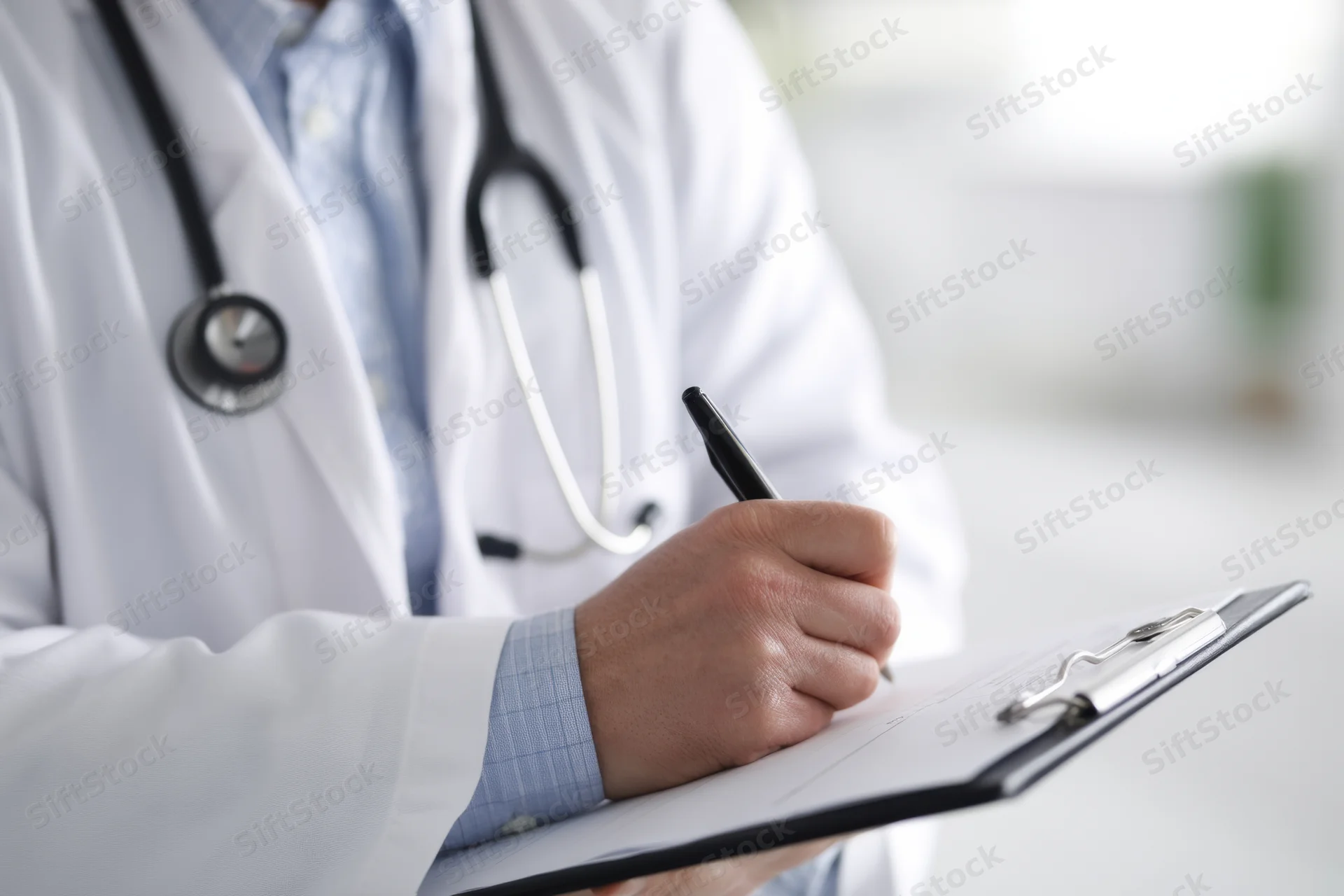 Doctor writing on clipboard with stethoscope around neck in clinic