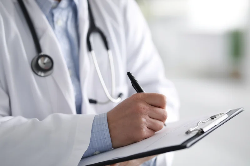 Doctor writing on clipboard with stethoscope around neck in clinic
