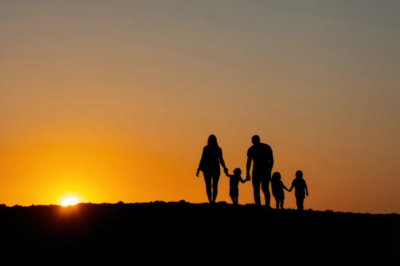 Family of five silhouetted walking along a ridge at sunset