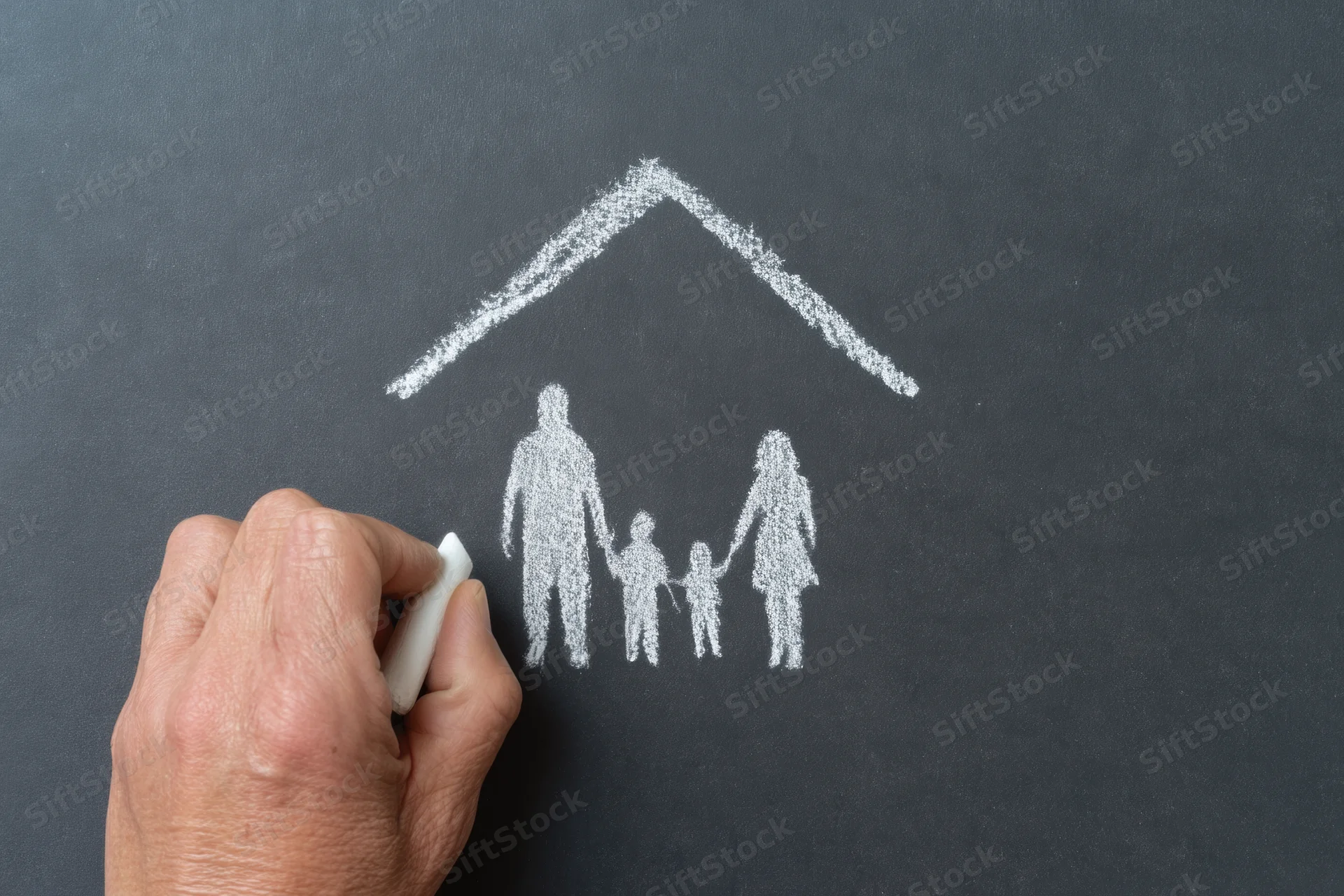 Hand drawing a chalk sketch of a family under a roof on a blackboard