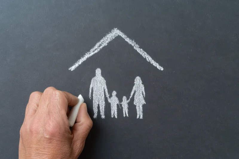 Hand drawing a chalk sketch of a family under a roof on a blackboard
