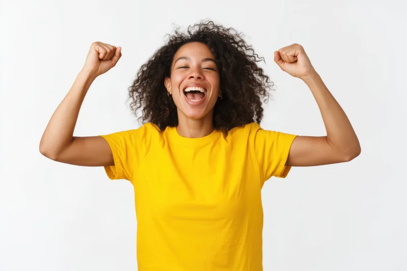 Woman celebrating with arms raised and fists clenched, wearing yellow tshirt, studio portrait