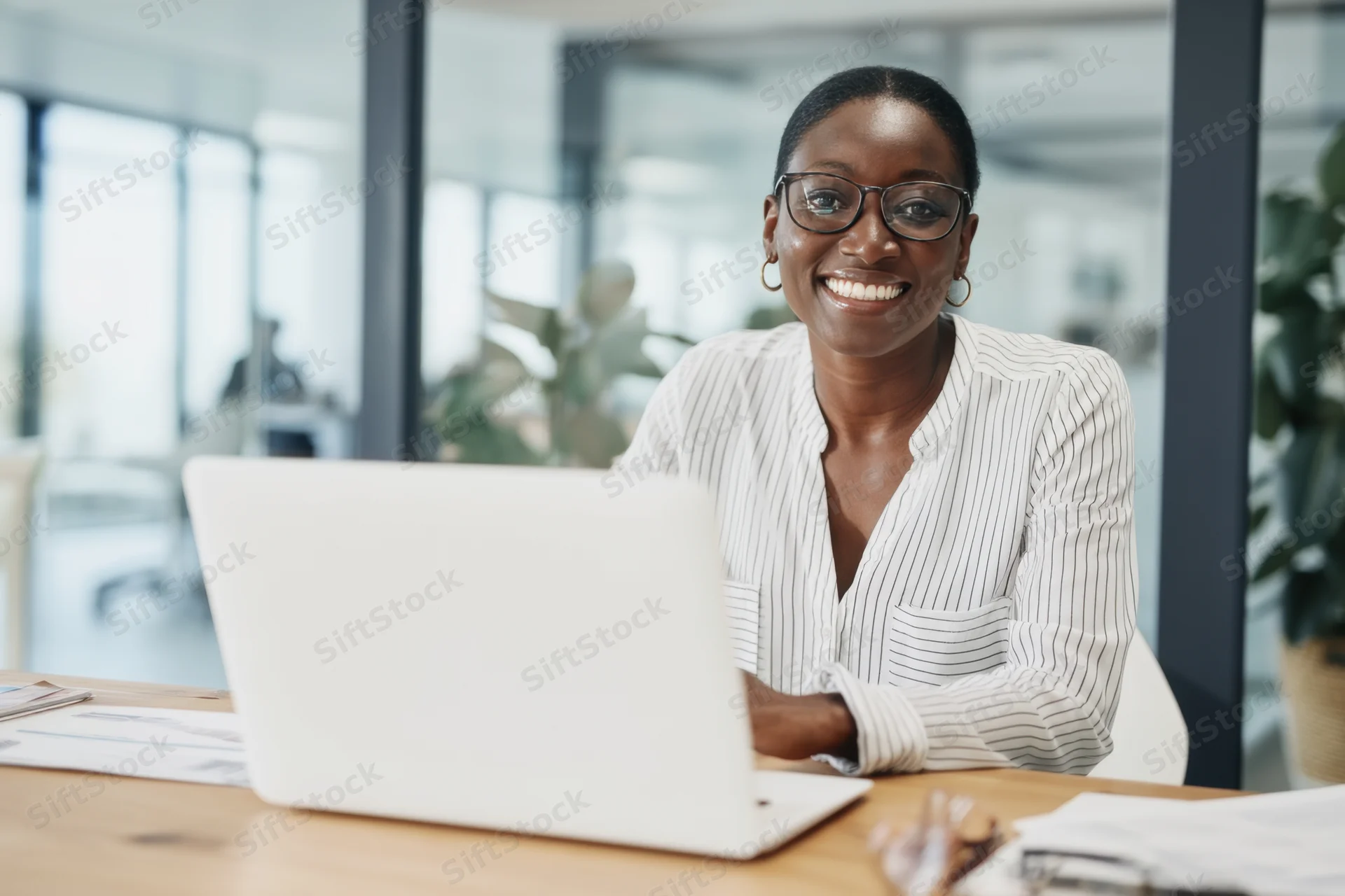 Woman smiling at camera while working on laptop at office desk