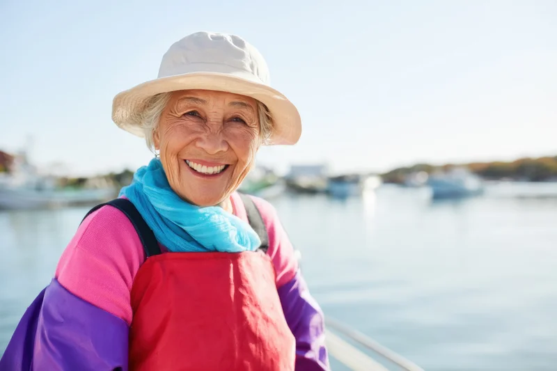 Smiling senior asian woman on a boat at a harbor wearing a hat and colorful clothing