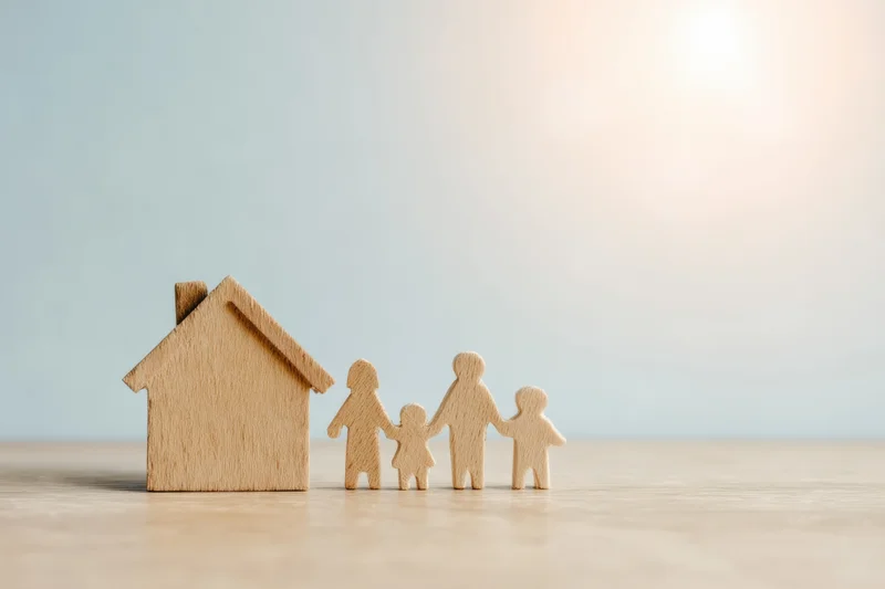 Wooden family figures standing beside a small house on a light wooden surface