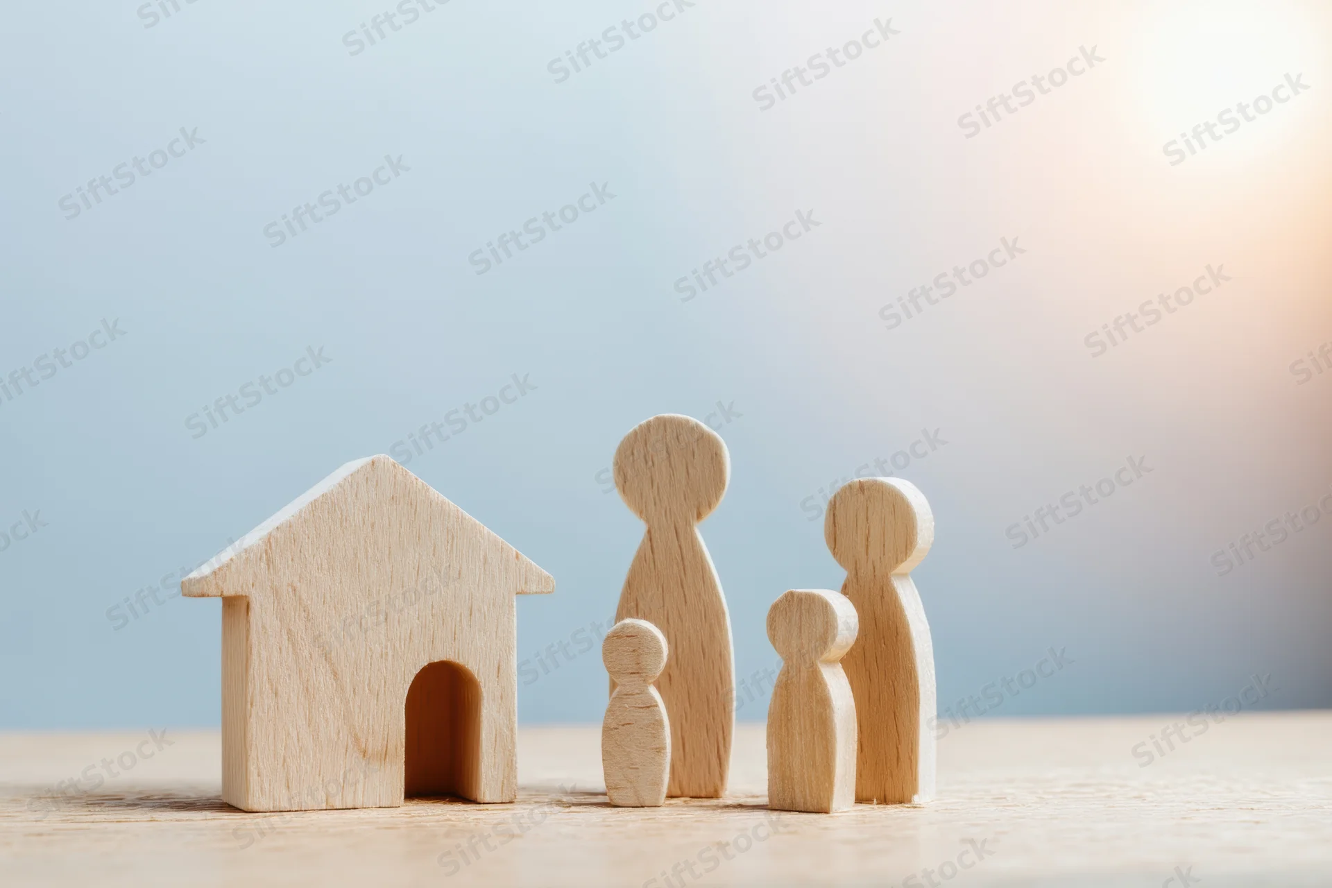 Wooden family figures and a house model on a light wooden surface with soft blue background