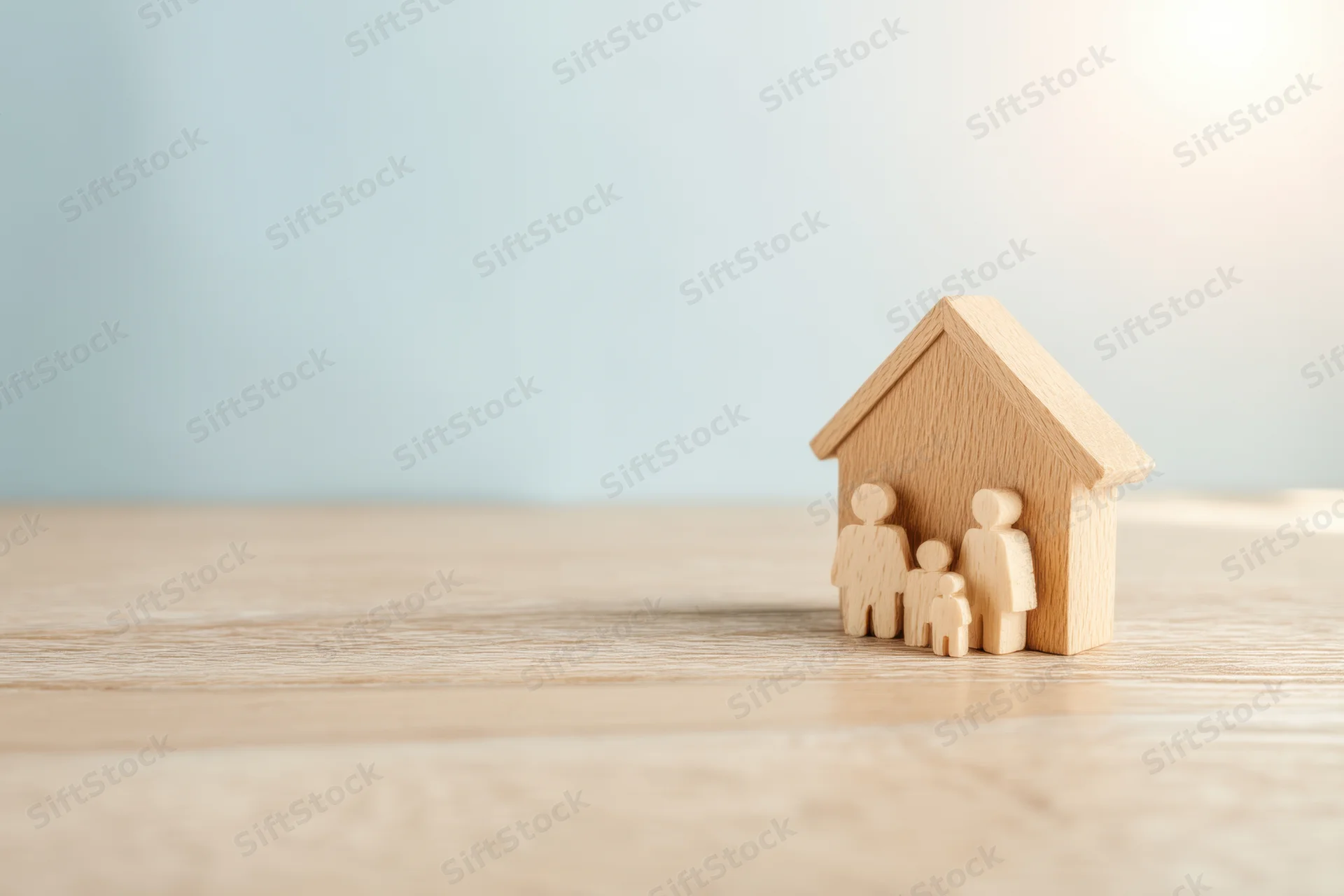 Wooden family figures standing beside a miniature house on a light wooden surface