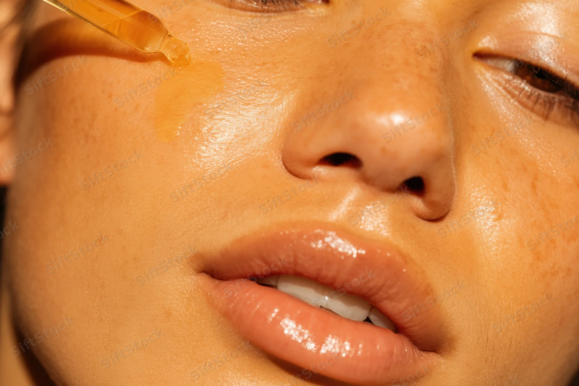 Close-up of a young woman applying serum to her face with a dropper
