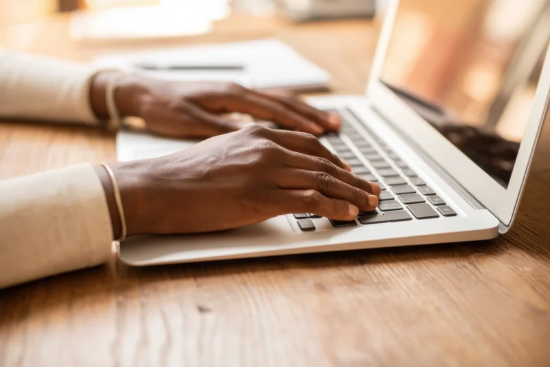 Close-up of hands typing on a silver laptop at a wooden desk
