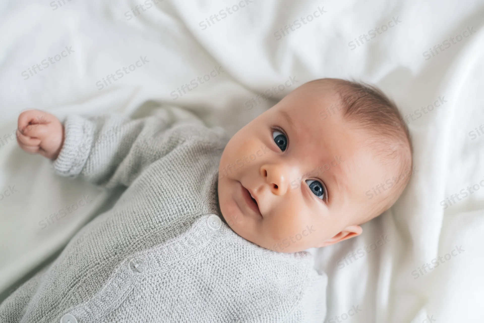 Baby lying on white blanket wearing gray knitted onesie